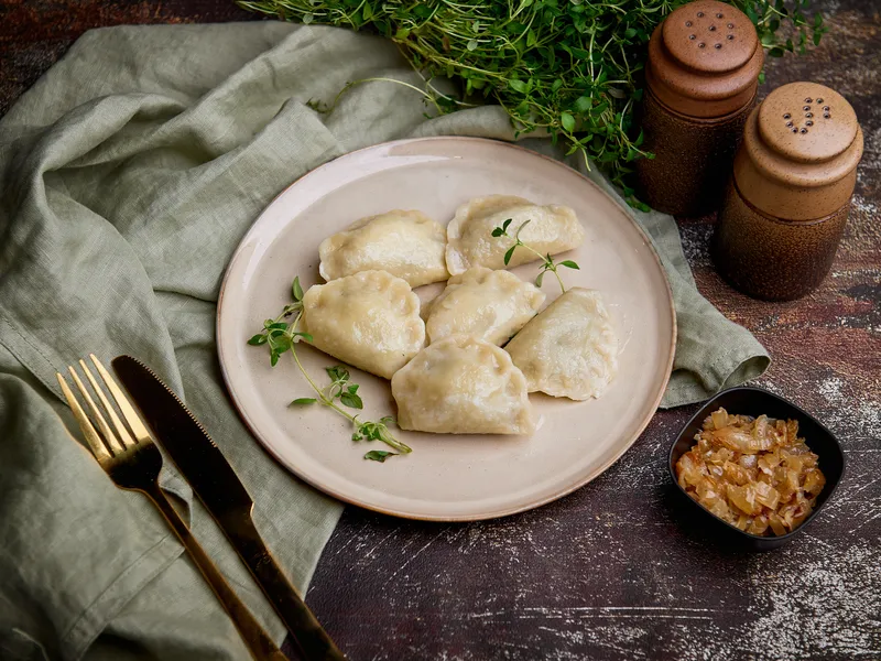 Pierogi ukraińskie Grube Pierogi na talerzu, obok miseczka podsmażonej cebulki